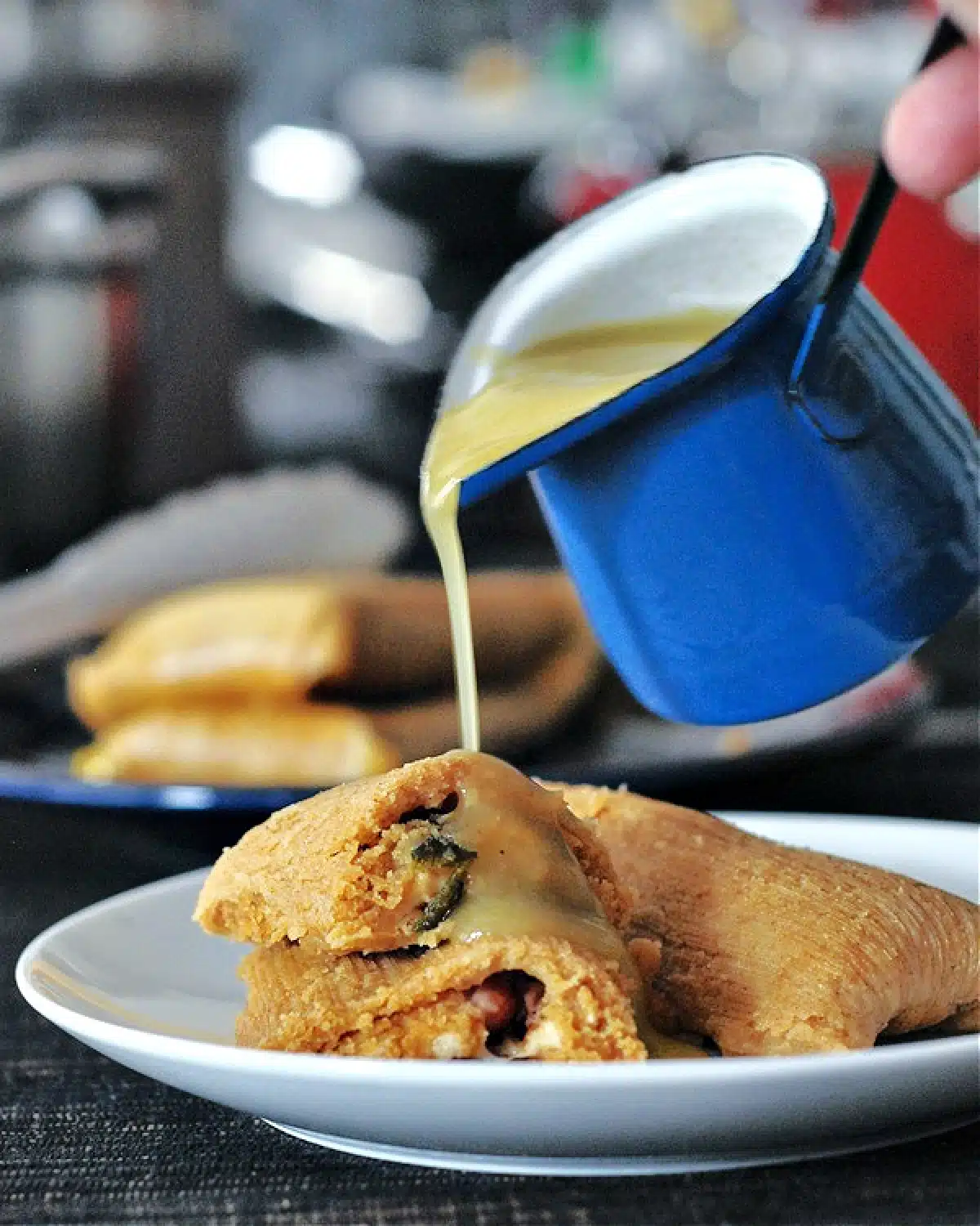 Homemade green enchilada sauce being poured from a small blue sauce ladle onto tamales.