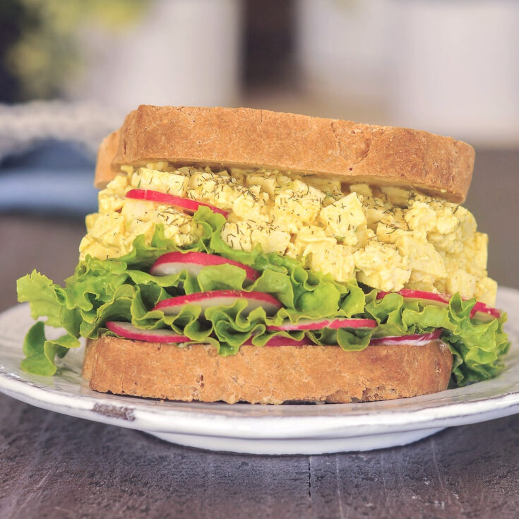 A vegan egg salad sandwich with curly green lettuce and bright red slices of radish.