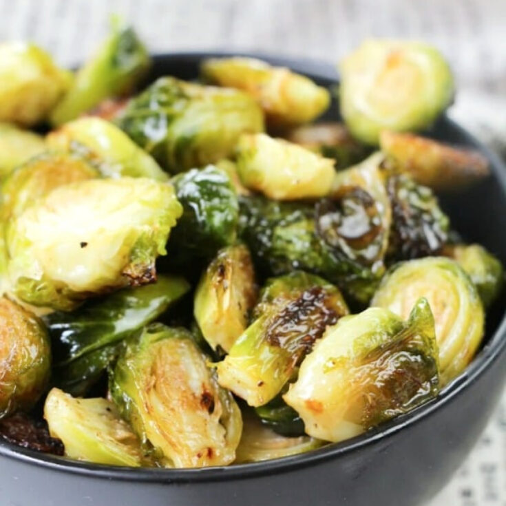 close up of bright green ginger lime Brussels sprouts in a black bowl with a newsprint napkin on the side