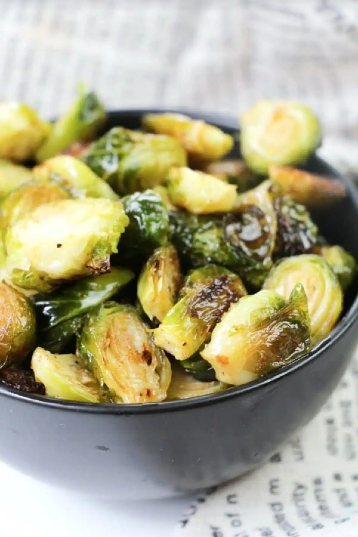 bright green ginger lime Brussels sprouts in a black bowl with a newsprint napkin on the side