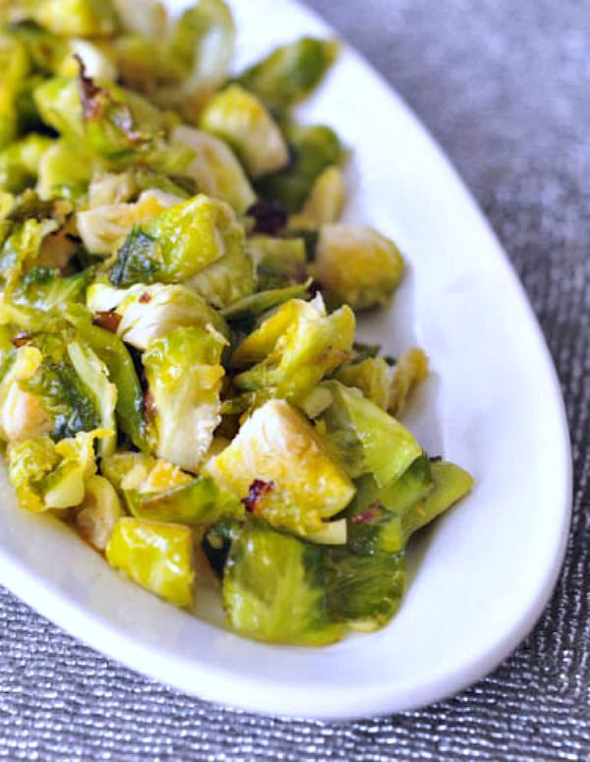 bright green ginger lime Brussels sprouts in a white oval platter on a silver beaded placemat.