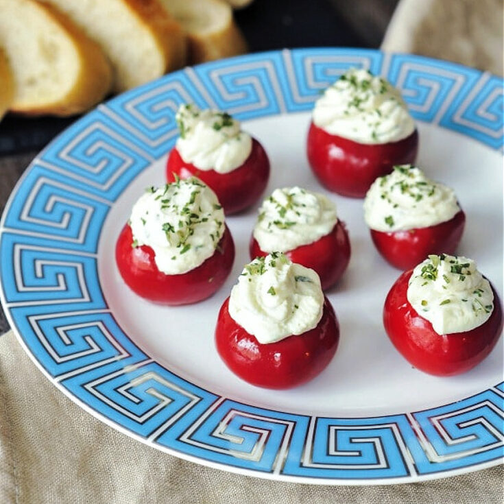 Round red peppadew sweet peppers filled with herb cheese (Boursin style) on a white plate with a light blue Greek Key border design