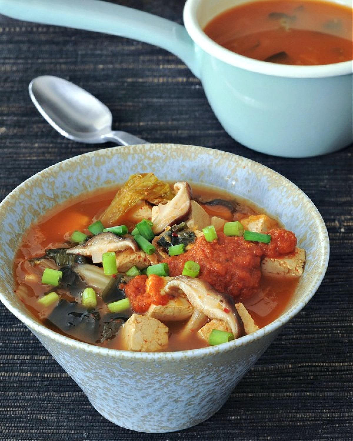 Bowl of instant kimchi noodle soup with tofu, mushrooms, broth, noodles, kimchi, scallions.