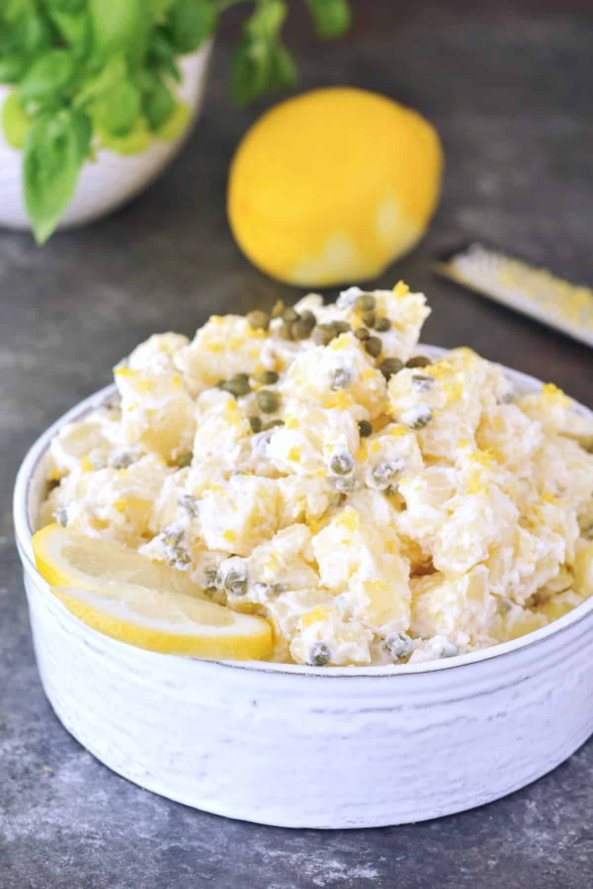 Lemon piccata potato salad in a serving bowl, garnished with a lemon slice, lemon zest, and capers