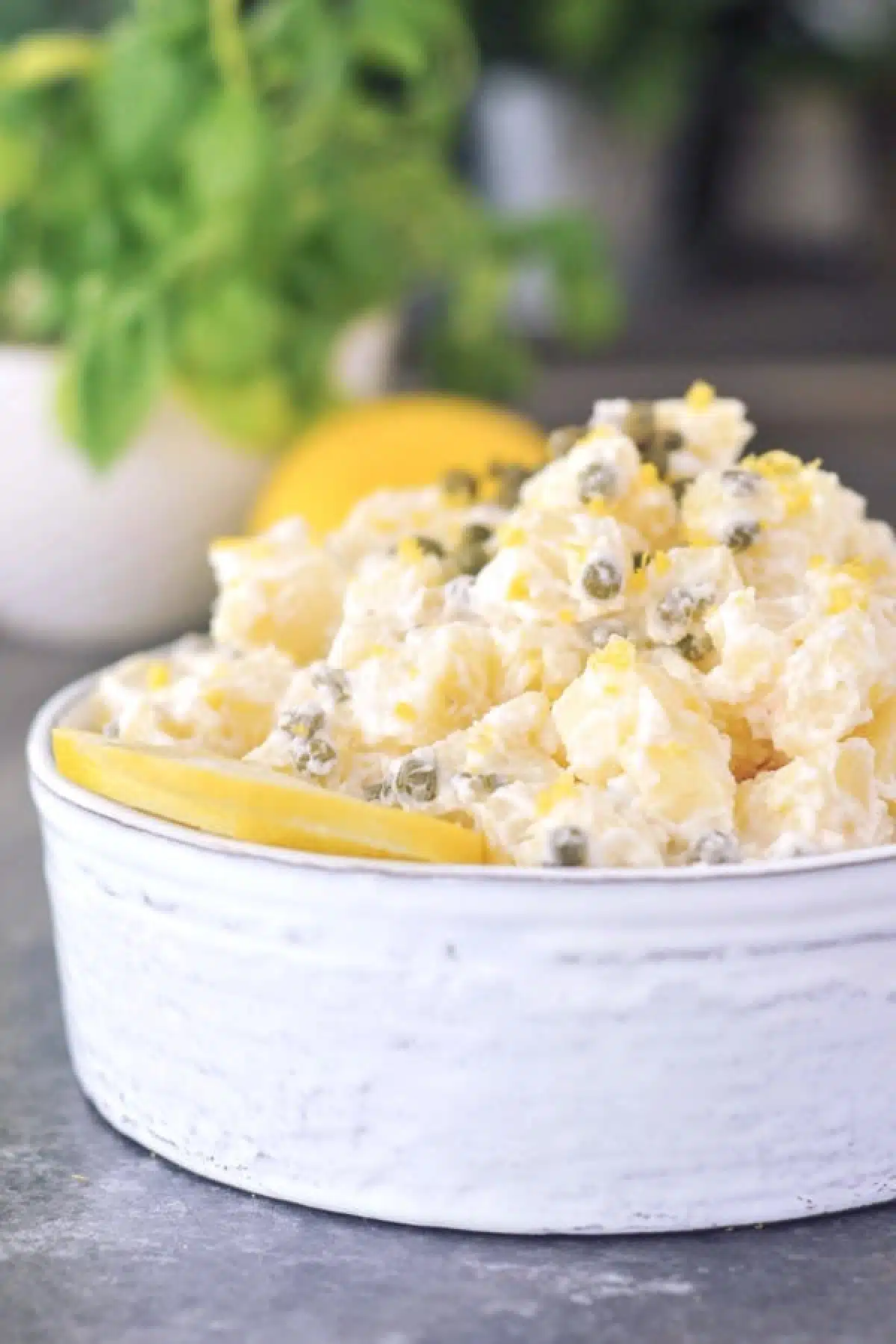 Lemon piccata potato salad in a serving bowl, garnished with a lemon slice, lemon zest, and capers