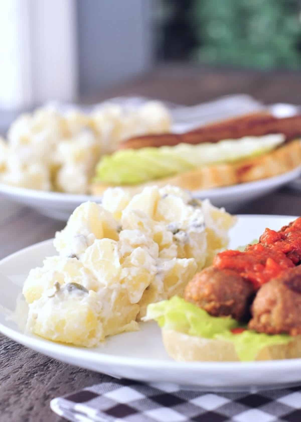 Lemon piccata potato salad served alongside potluck items: hot dogs, greens, hot sauce