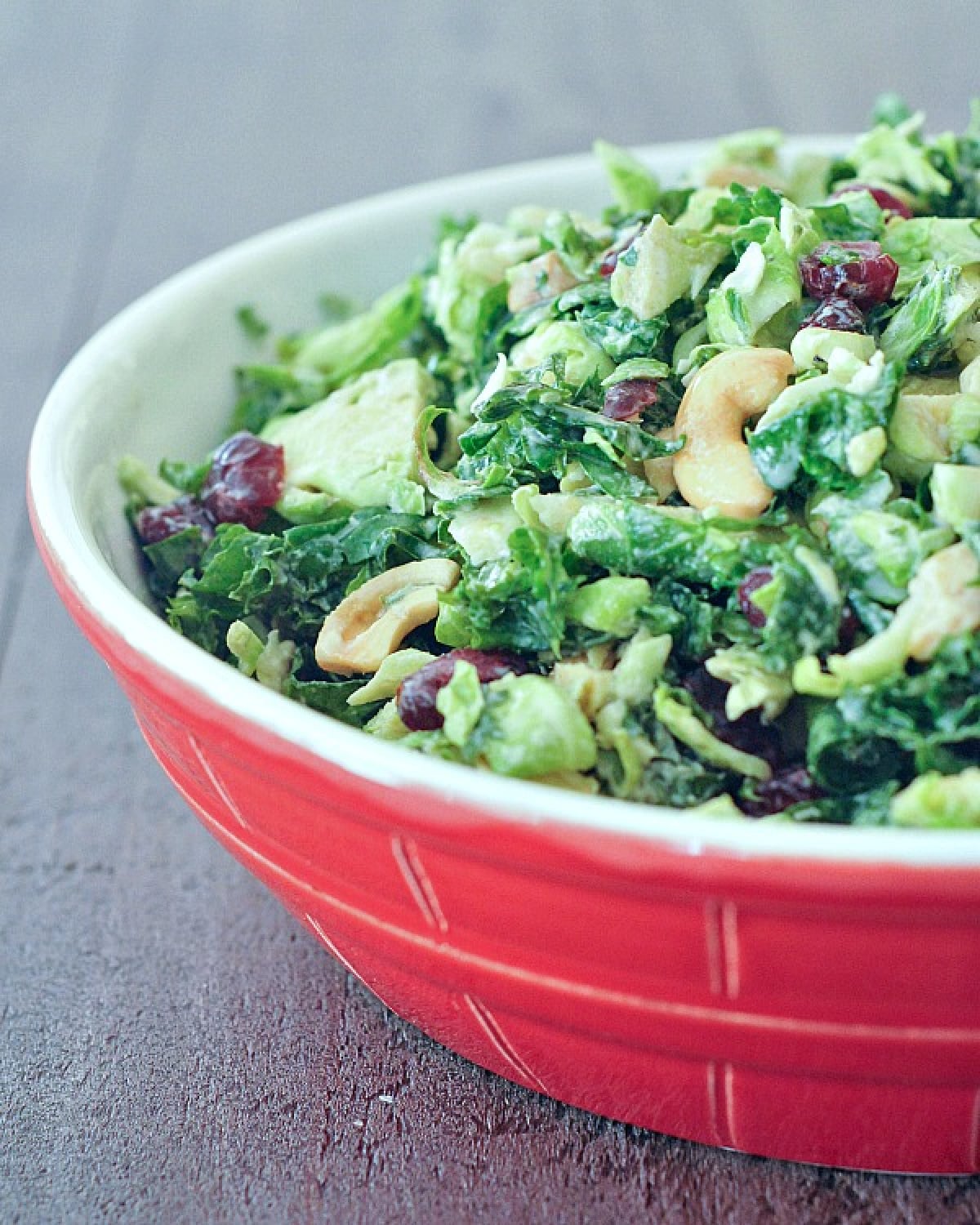 Lemon brussels and kale salad with cashews and dried cranberries in a large red serving bowl