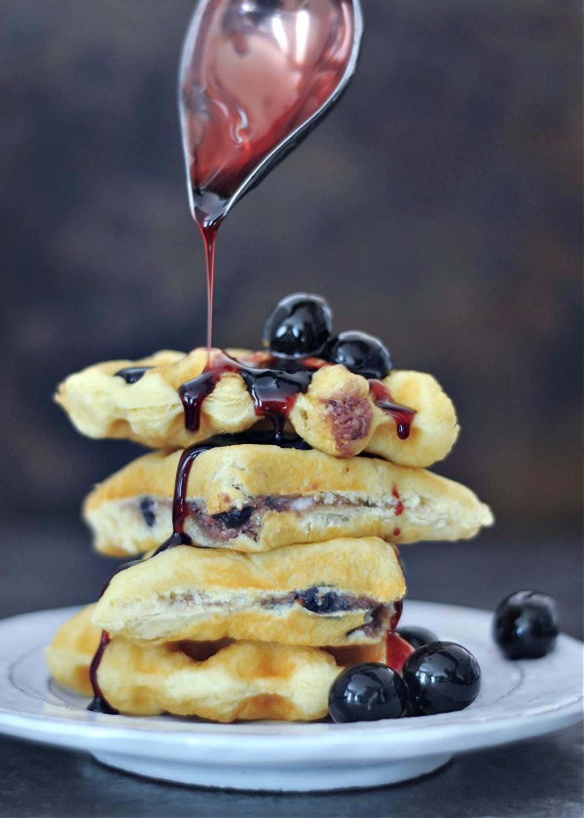 Luxardo cheesecake stuffed waffles stacked on a plate, cherry syrup being poured over top.