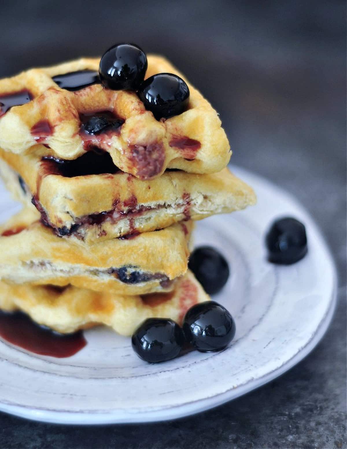 Luxardo cheesecake stuffed waffles stacked on a plate with cherries and syrup.