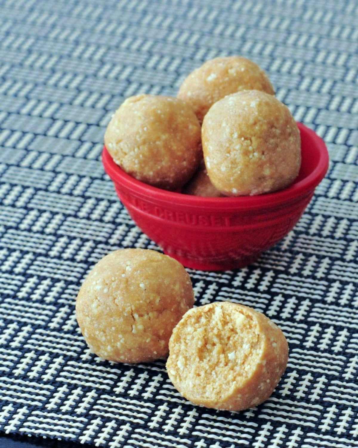 Small round orange creamsicle protein bites stacked in a small red bowl. two bites sitting outside the bowl, one with a slice out of it.