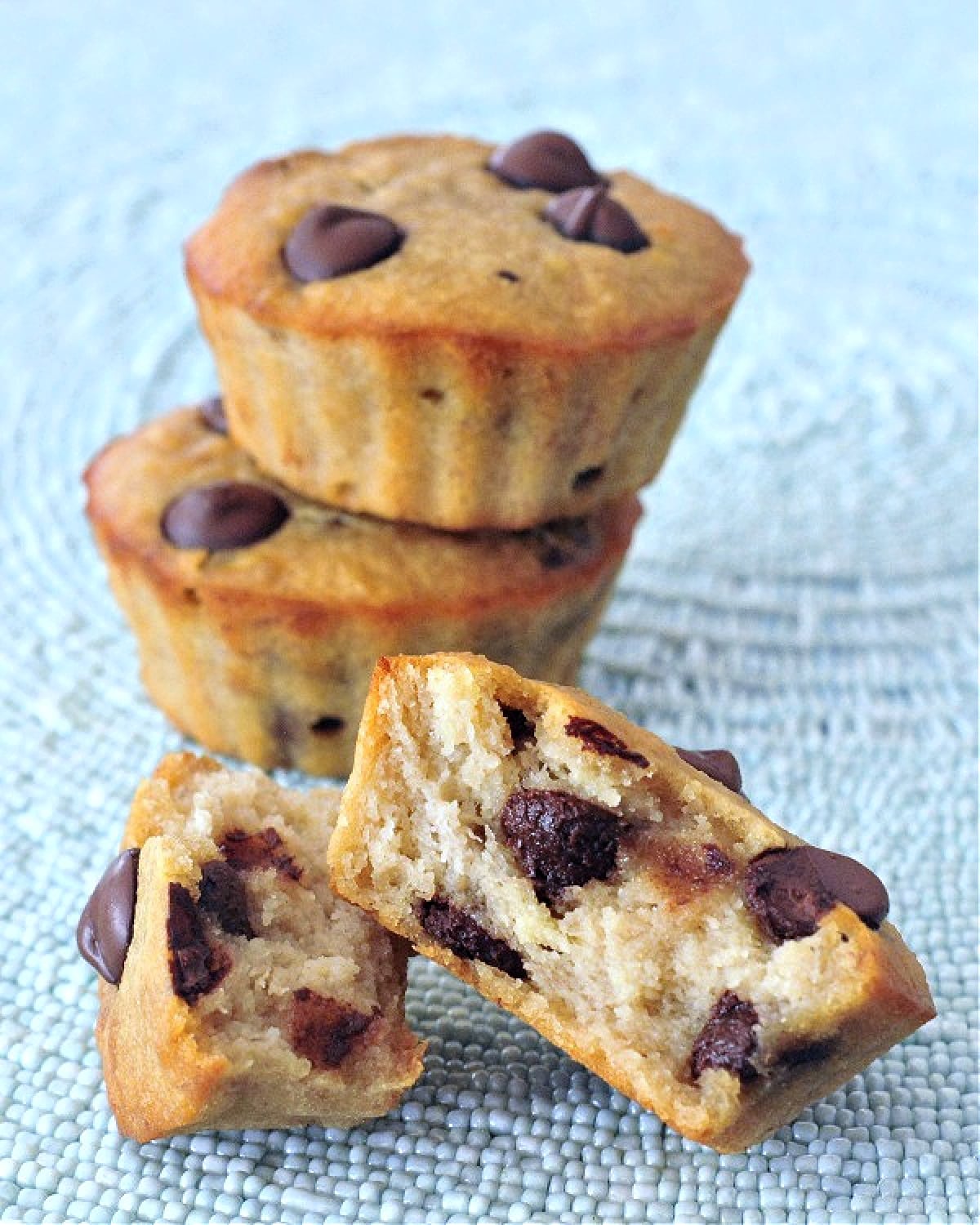 Three peanut butter chocolate chip muffins, one stacked on another, and one cut in half to show crumb inside.