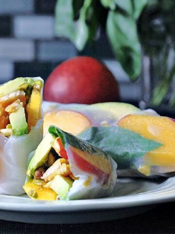 Summer rolls on a light green plate (summer rolls are pan fried tempeh, sliced nectarines, sliced avocado, fresh basil leaves, and pistachios rolled in softened rice paper).