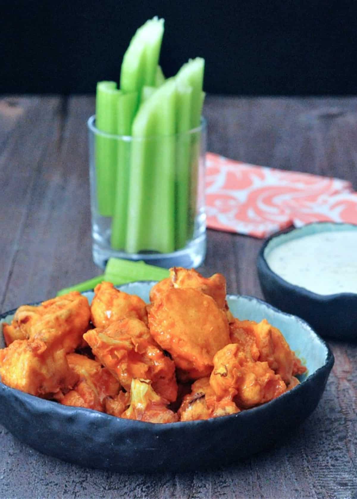 Vegan air fryer buffalo cauliflower served in a bowl with celery and ranch dressing on the side.