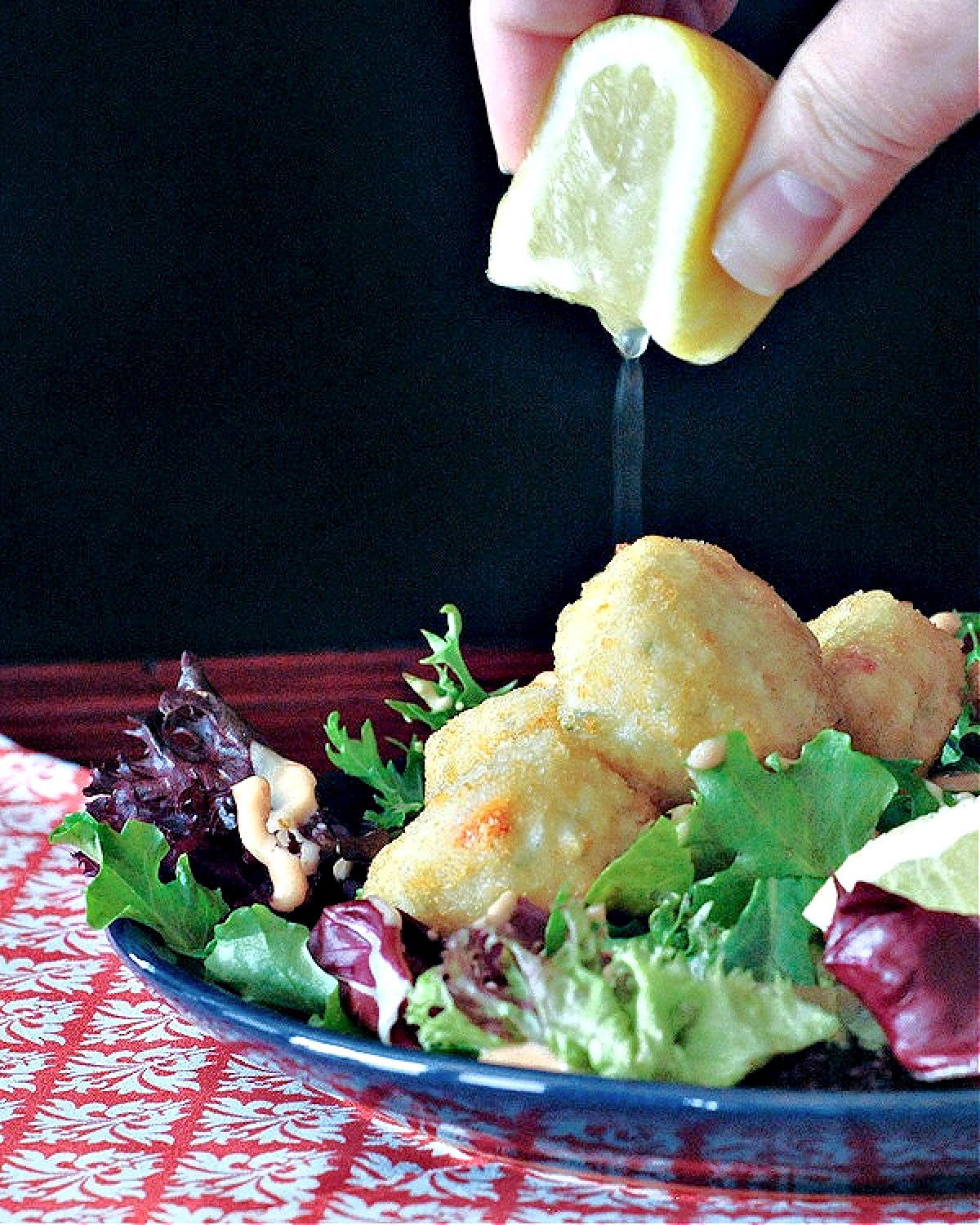 An entree salad of greens, crab cakes, and Thousand Island dressing; a hand squeezing a lemon over the salad.