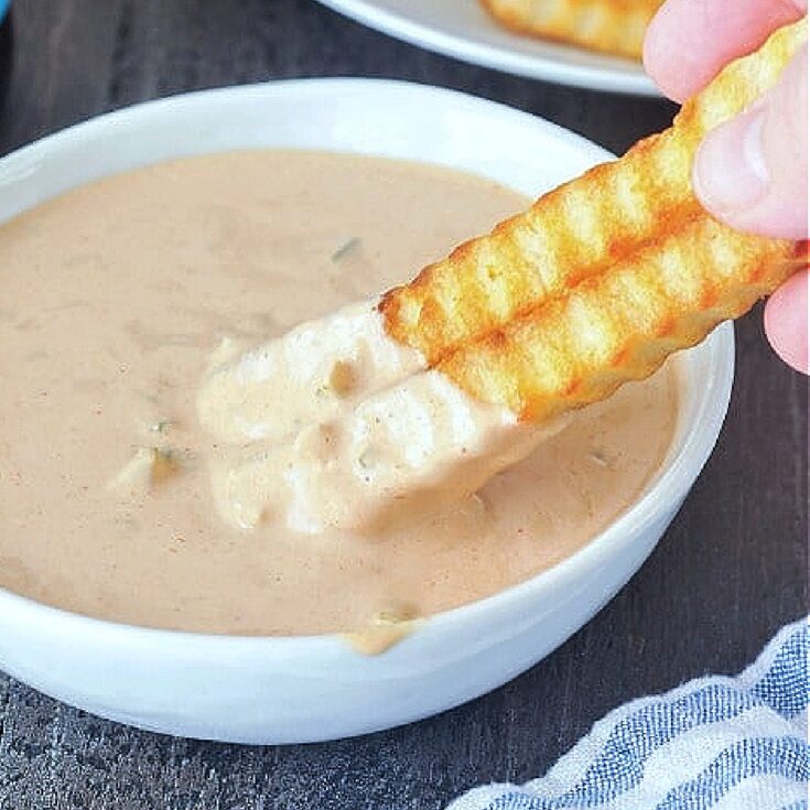 Close up of krinkle cut French fries being dipped into a bowl of Thousand Island dressing.