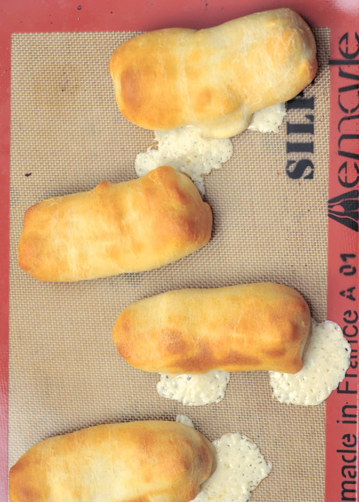 Overhead view of four hot dogs with cheese wrapped in baked pastry on a baking sheet, melted cheese dripping out the sides.