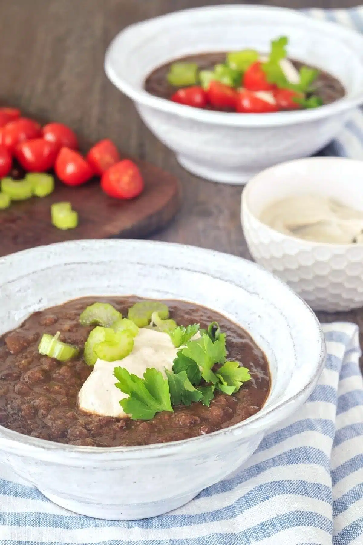 Chipotle Black Bean Soup in bowls, garnished with cherry tomatoes, cashew cream, and green parsley.