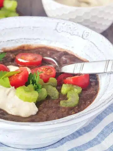 Chipotle Black Bean Soup in a bowl, garnished with cherry tomatoes, cashew cream, and green parsley.