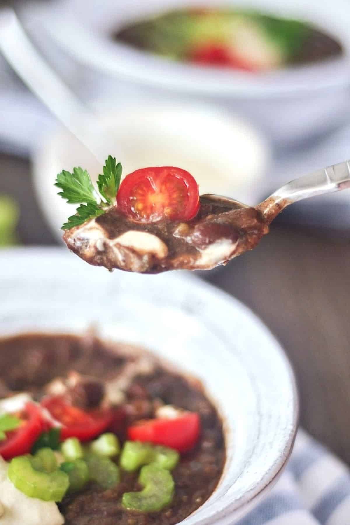 closeup of a spoonful of Chipotle Black Bean Soup with a tomato and parsley leaf garnish.