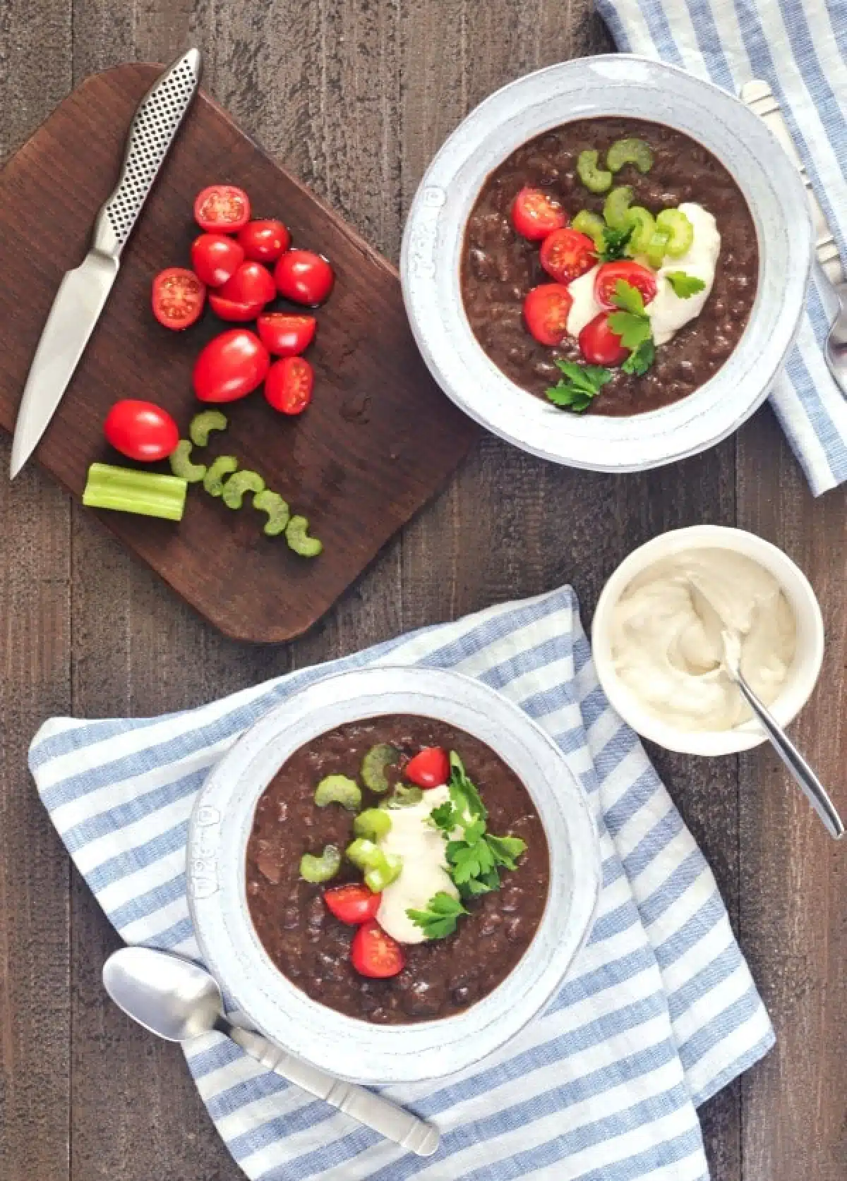 Overhead view of Chipotle Black Bean Soup in bowls, garnished with cherry tomatoes, cashew cream, and green parsley.