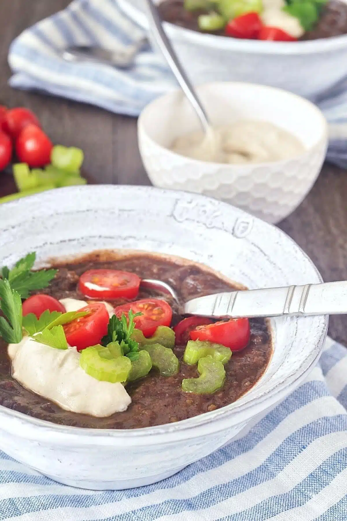 Chipotle Black Bean Soup in bowls, garnished with cherry tomatoes, cashew cream, and green parsley.