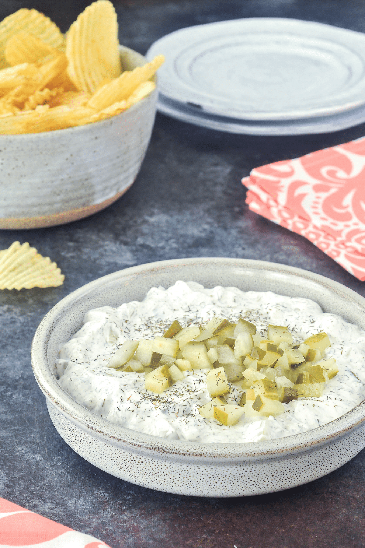 Dill pickle dip in a shallow bowl, with a second bowl of ruffled potato chips for dipping.