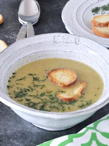 Artichoke soup in bowls garnished with crisp bagel chips and chopped herbs.