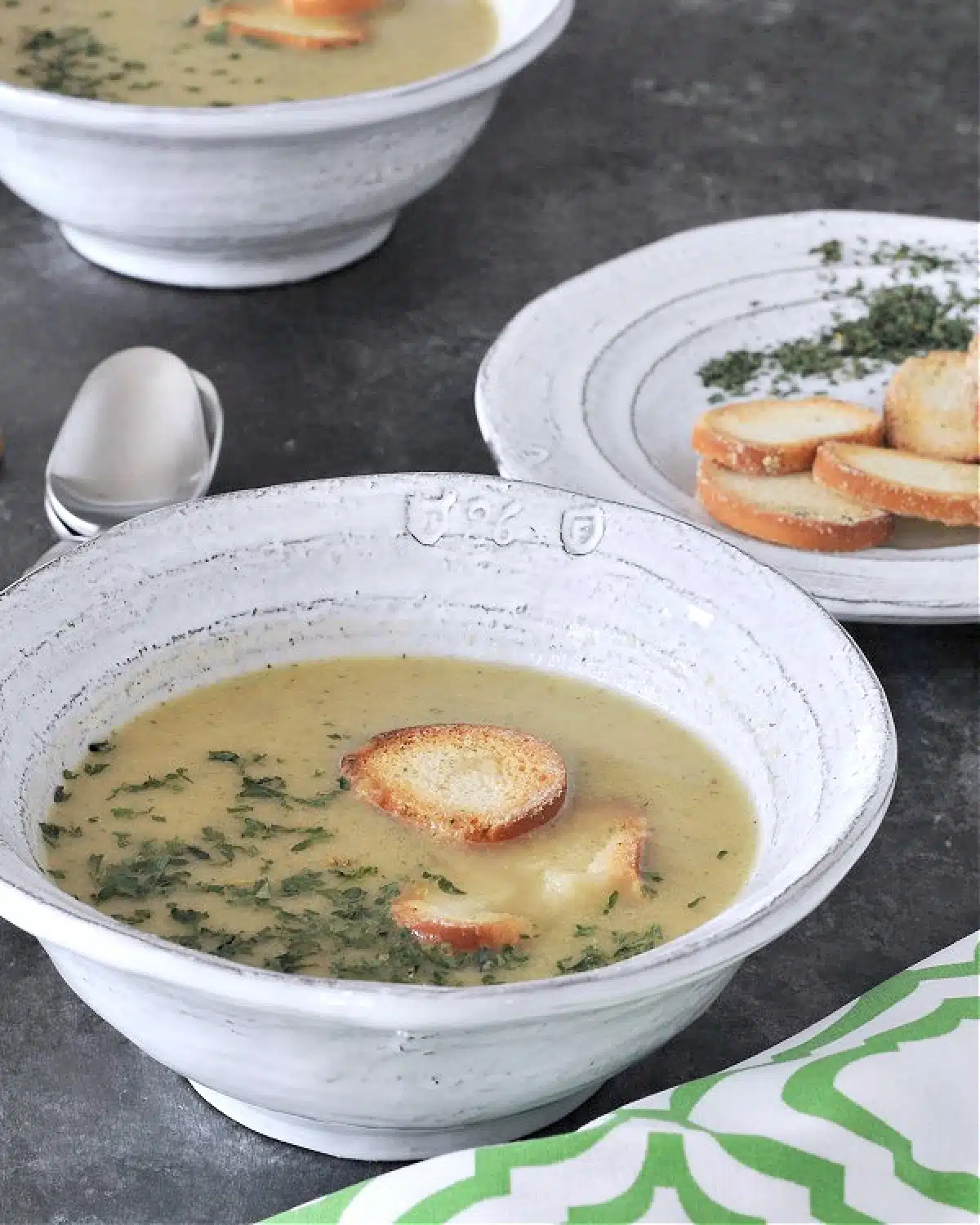 Artichoke soup in bowls garnished with crisp bagel chips and chopped herbs.