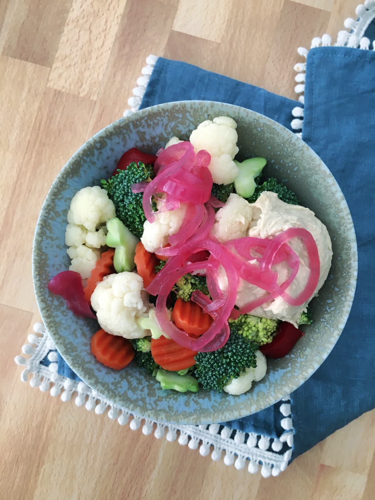 Overhead view of a rustic grey bowl filled with pickled vegetables: cucumber and broccoli trees, sliced carrot, pink onion slices, cucumber.