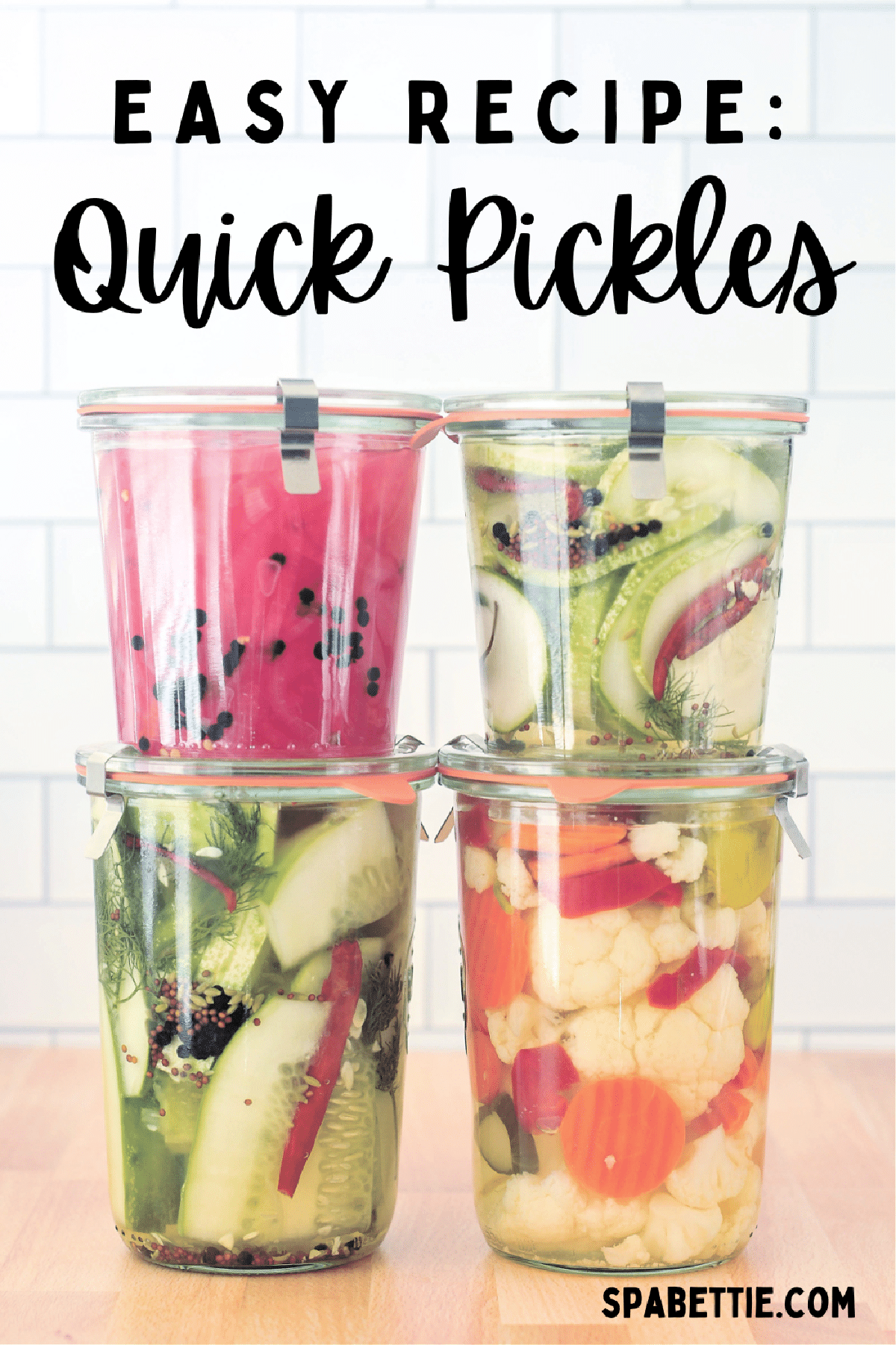 Four glass jars stacked two high, filled with quick pickles: a small jar of bright pink pickled onions sits on a larger jar of quick pickles, and a smaller jar of quick pickles sits on a larger jar of pickled carrot, cauliflower, and peppers.
