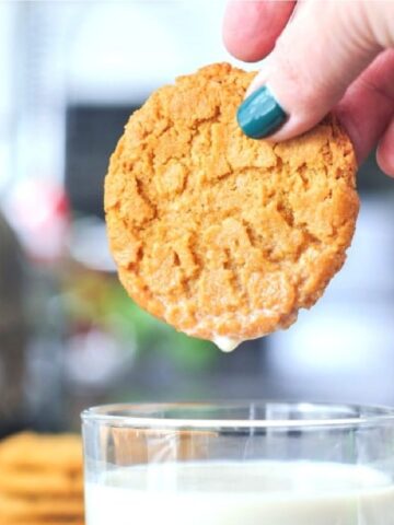 A hand dunking a flourless almond butter cookie into a glass of milk.