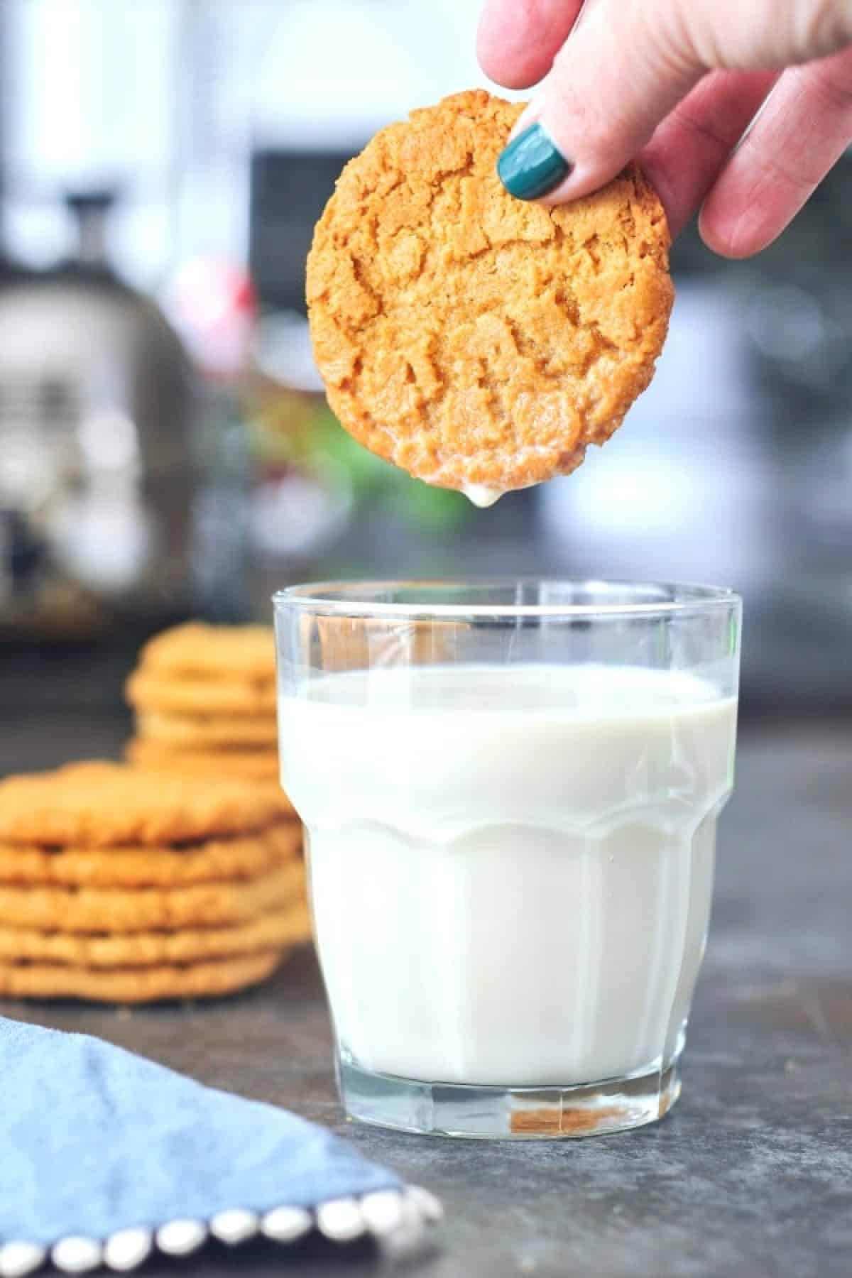 A hand dunking a flourless almond butter cookie into a glass of milk.
