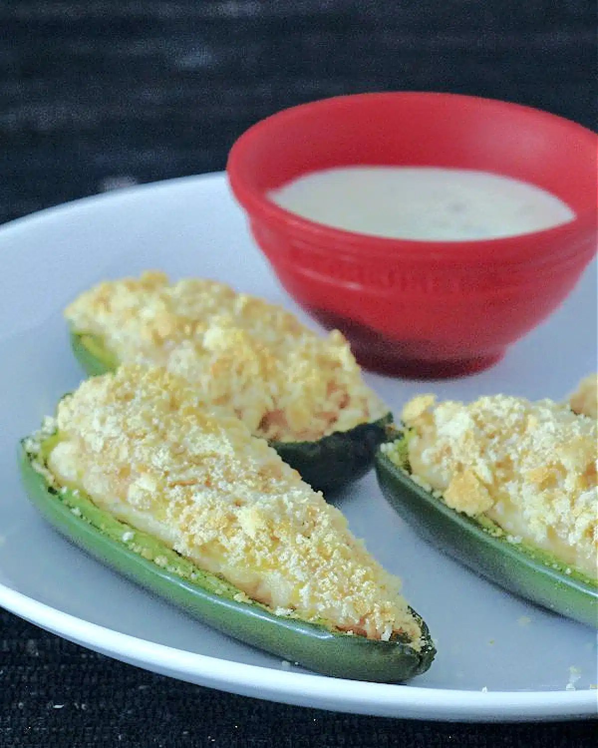 close up of Pineapple Jalapeño Poppers on a white plate with a small red bowl of ranch dressing on the side.