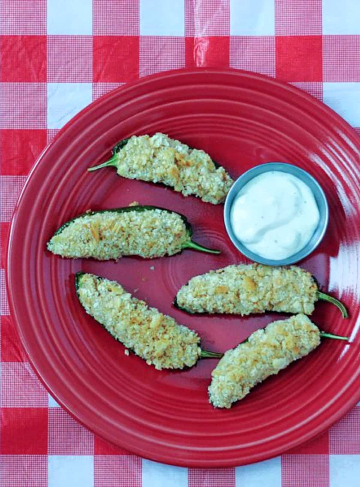 Overhead view of pineapple jalapeño poppers on a red plate with a small silver bowl of ranch dipping sauce.