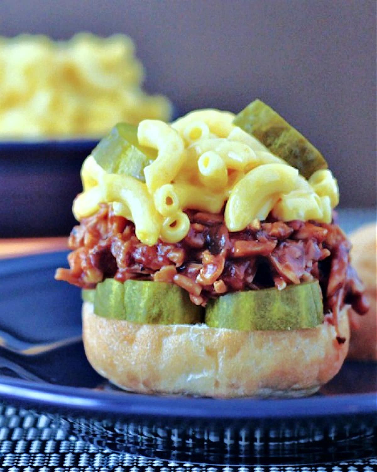 A vegan pulled pork made with porcini mushrooms in a slider bun with pickle slices and mac and cheese.