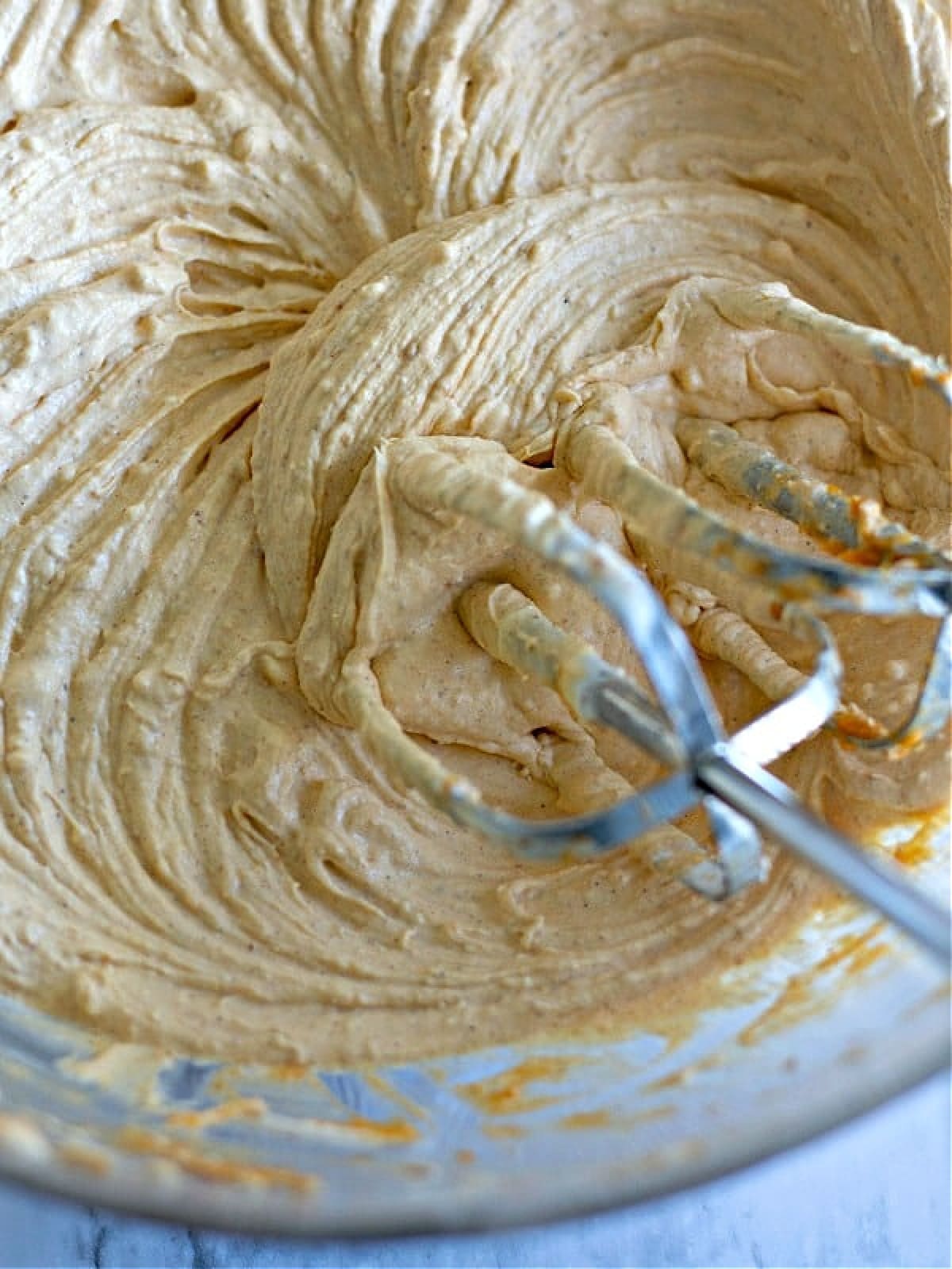 Pumpkin cheesecake dip in a large glass bowl, with mixer beaters in it, whipped texture on surface of dip.