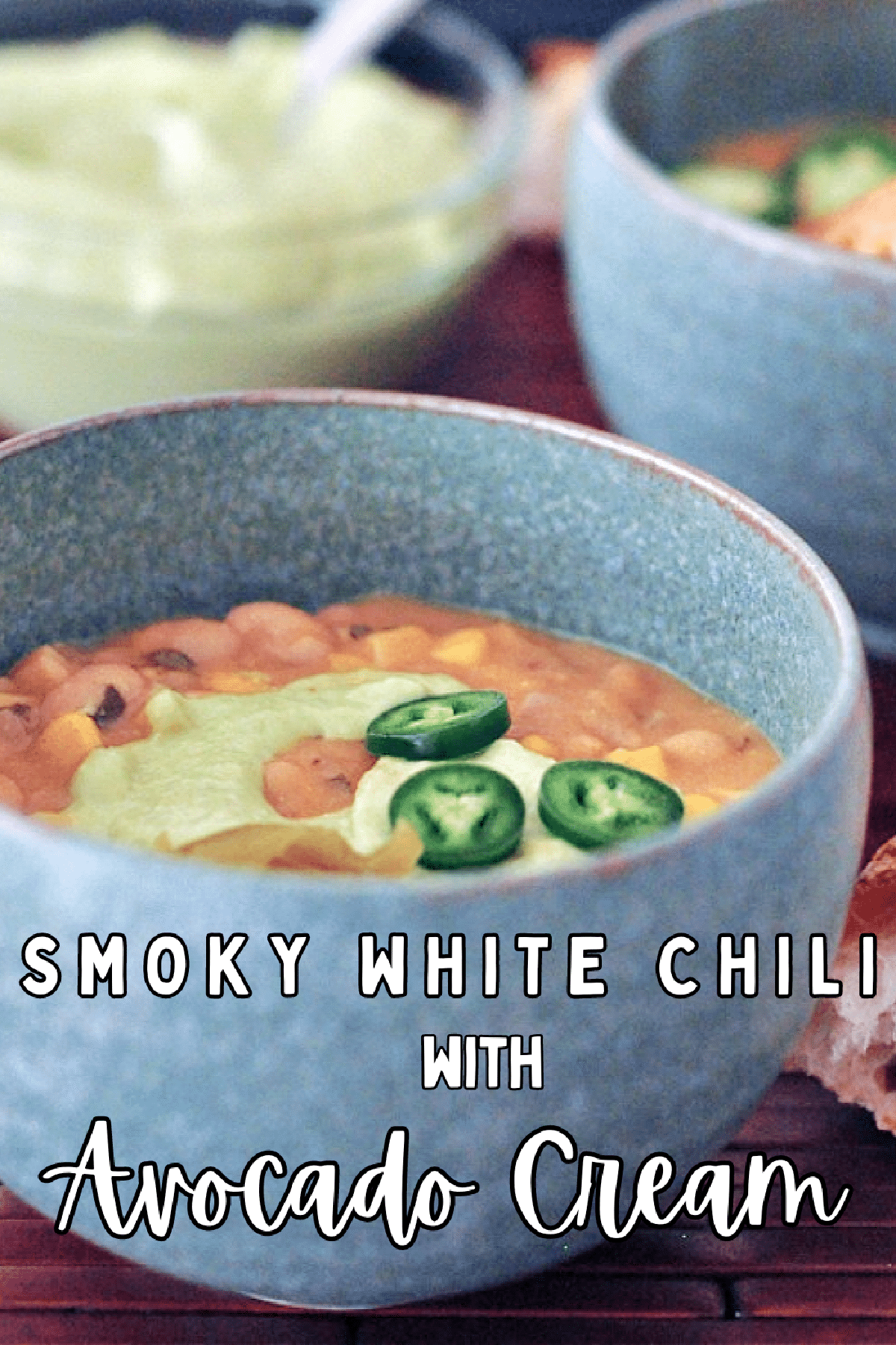 White bean chili in a grey bowl, garnished with light green Hatch avocado cream and sliced jalapeno peppers.