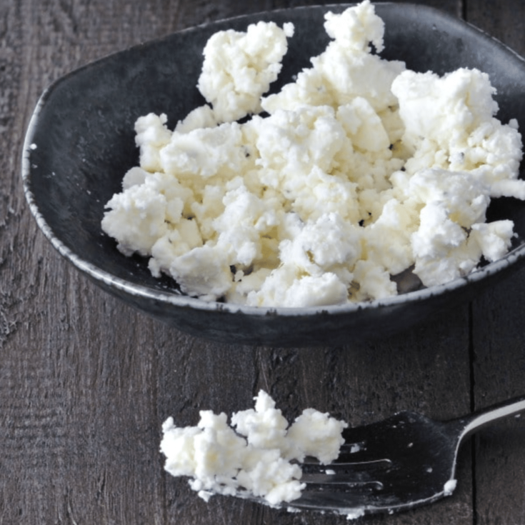 Crumbled vegan goat cheese in a dark grey bowl, with a forkful of goat cheese on the side.