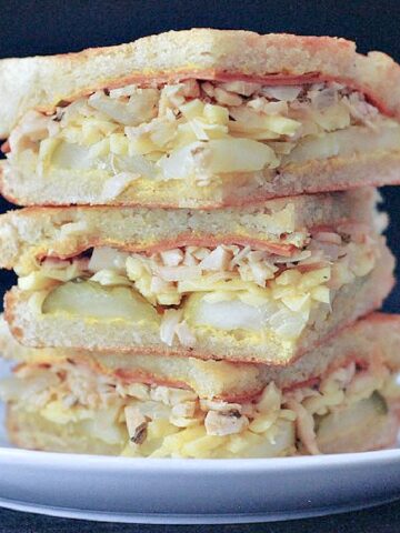 Close up of a vegan Cubano sandwich sliced into triangles and stacked on a white plate against a black background.