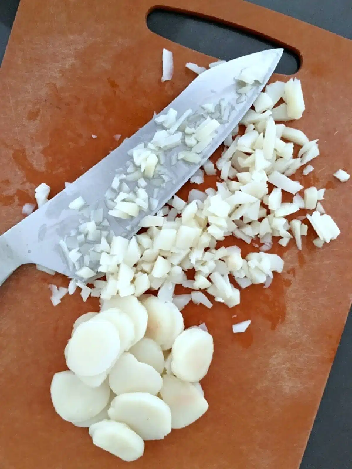 Chopped water chestnuts on cutting board with knife.