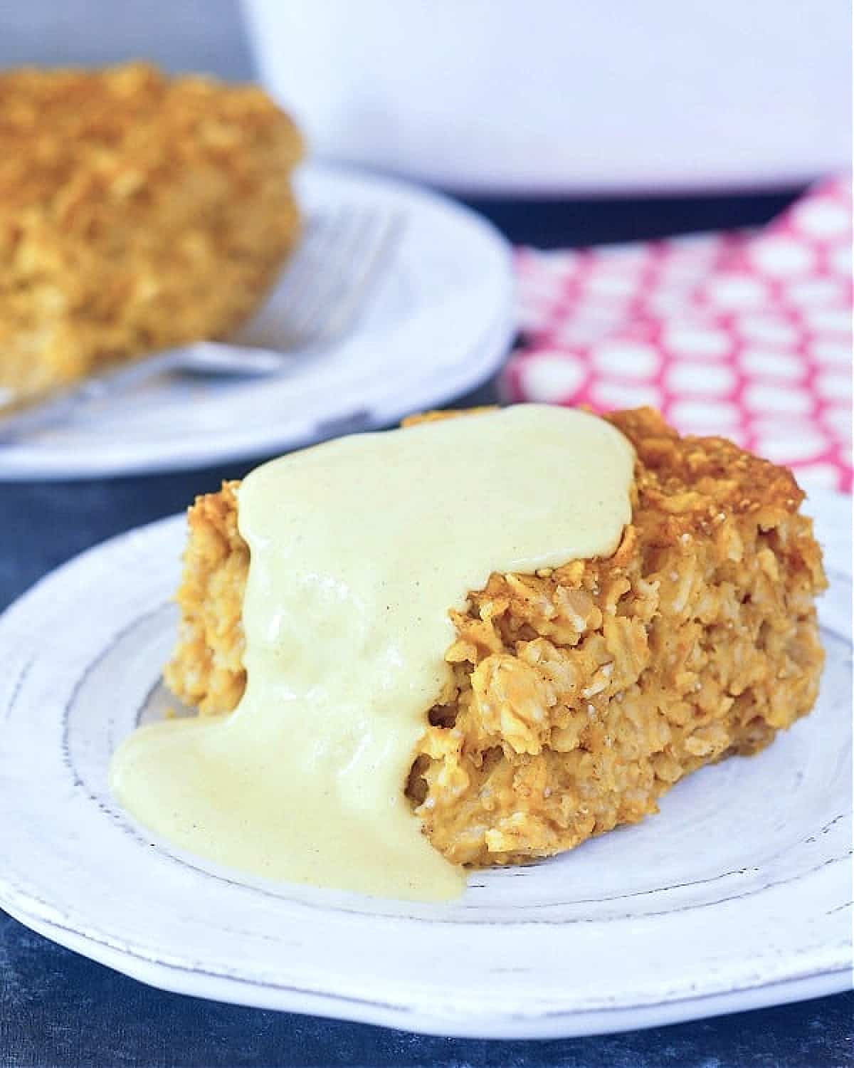 A square slice of baked pumpkin oatmeal on a rustic grey dish, with golden cashew cream on top.