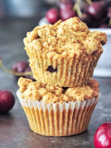 Two cherry zucchini muffins stacked one on top of another, with a bowl of fresh cherries in the background.