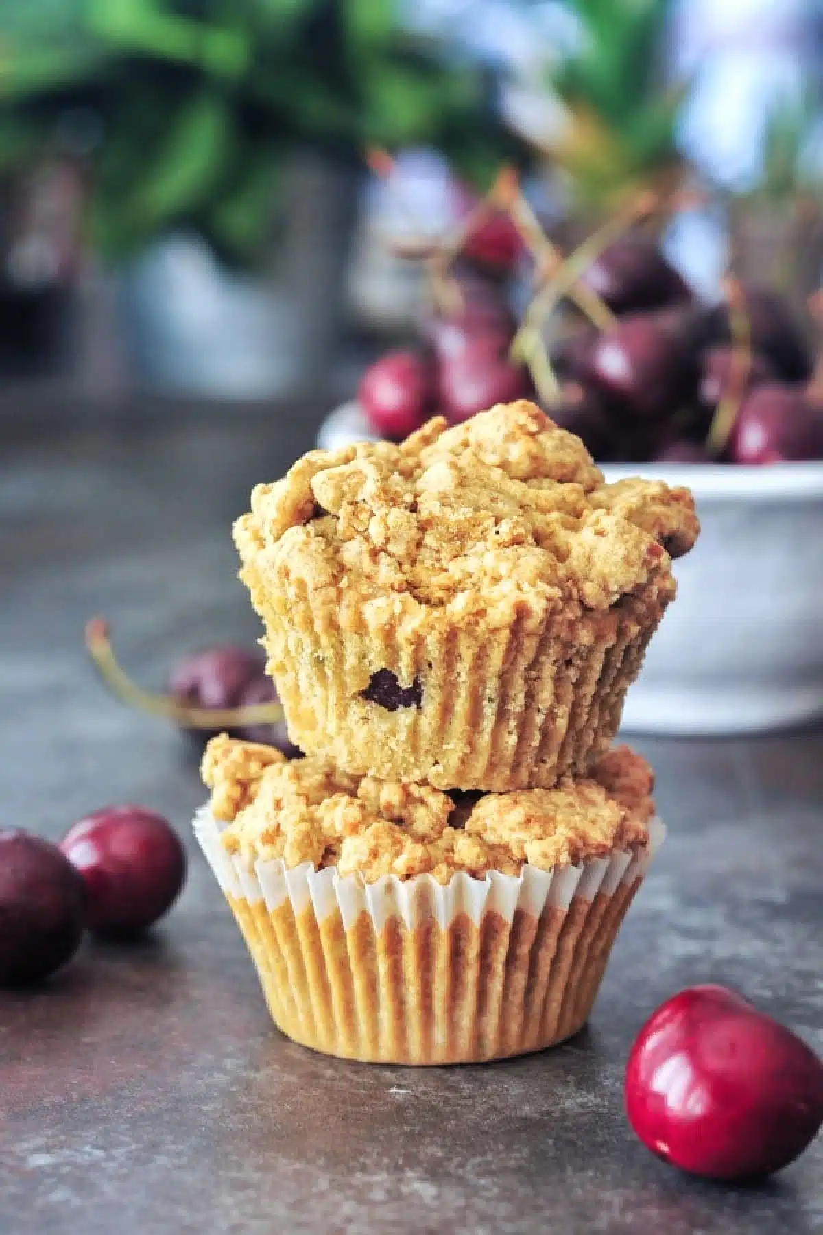 Two cherry zucchini muffins stacked one on top of another, with a bowl of fresh cherries in the background.