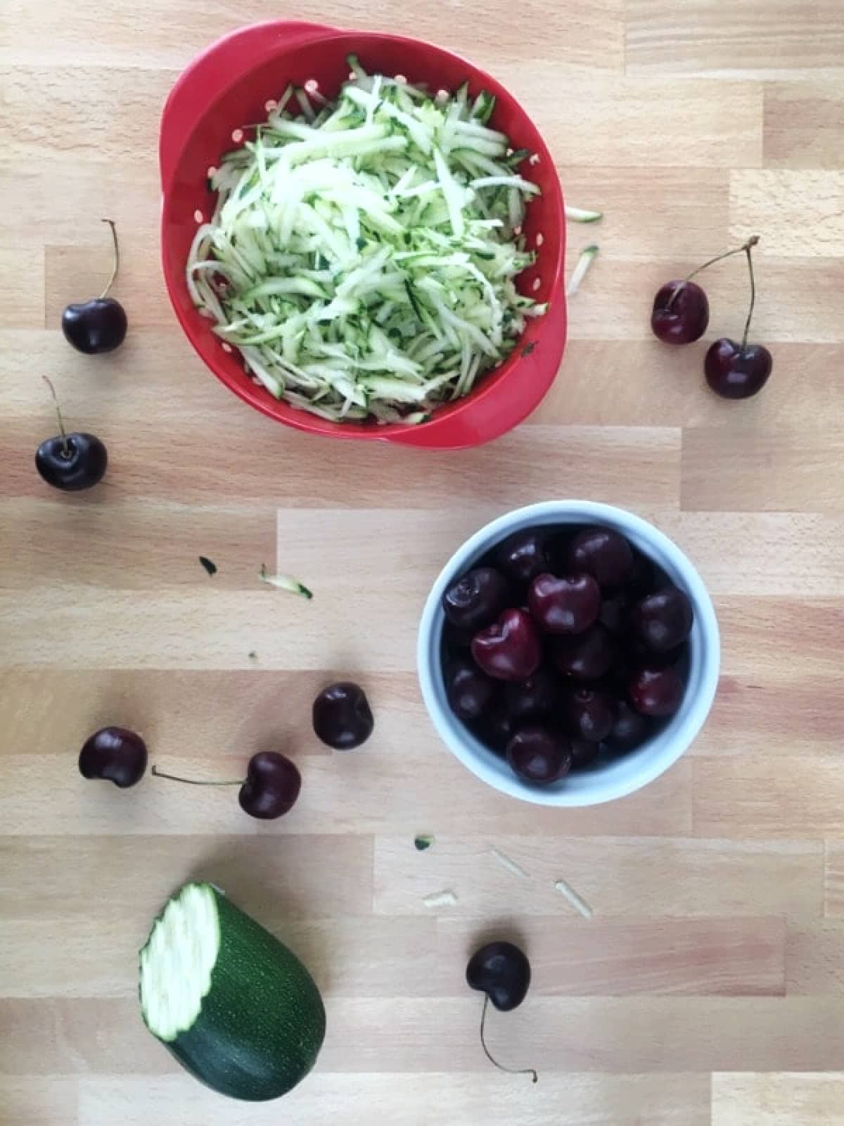 How to make cherry zucchini muffins: bowls of fresh grated zucchini and pitted cherries on a butcher block.