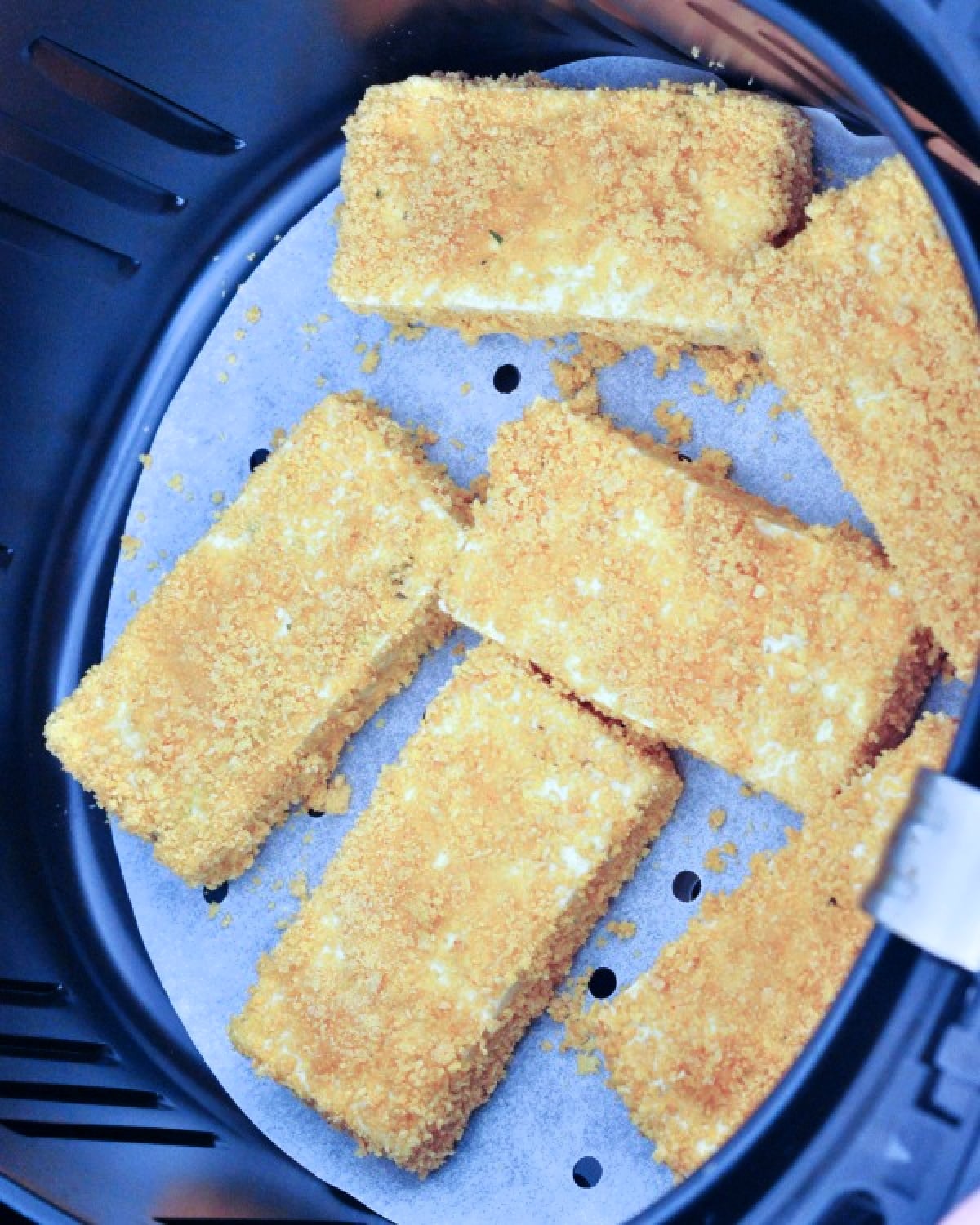 Several slices of crispy fried tofu on parchment inside an air fryer basket.