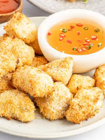 A rustic white plate of crispy breaded tofu with a smaller white bowl of dipping sauce.