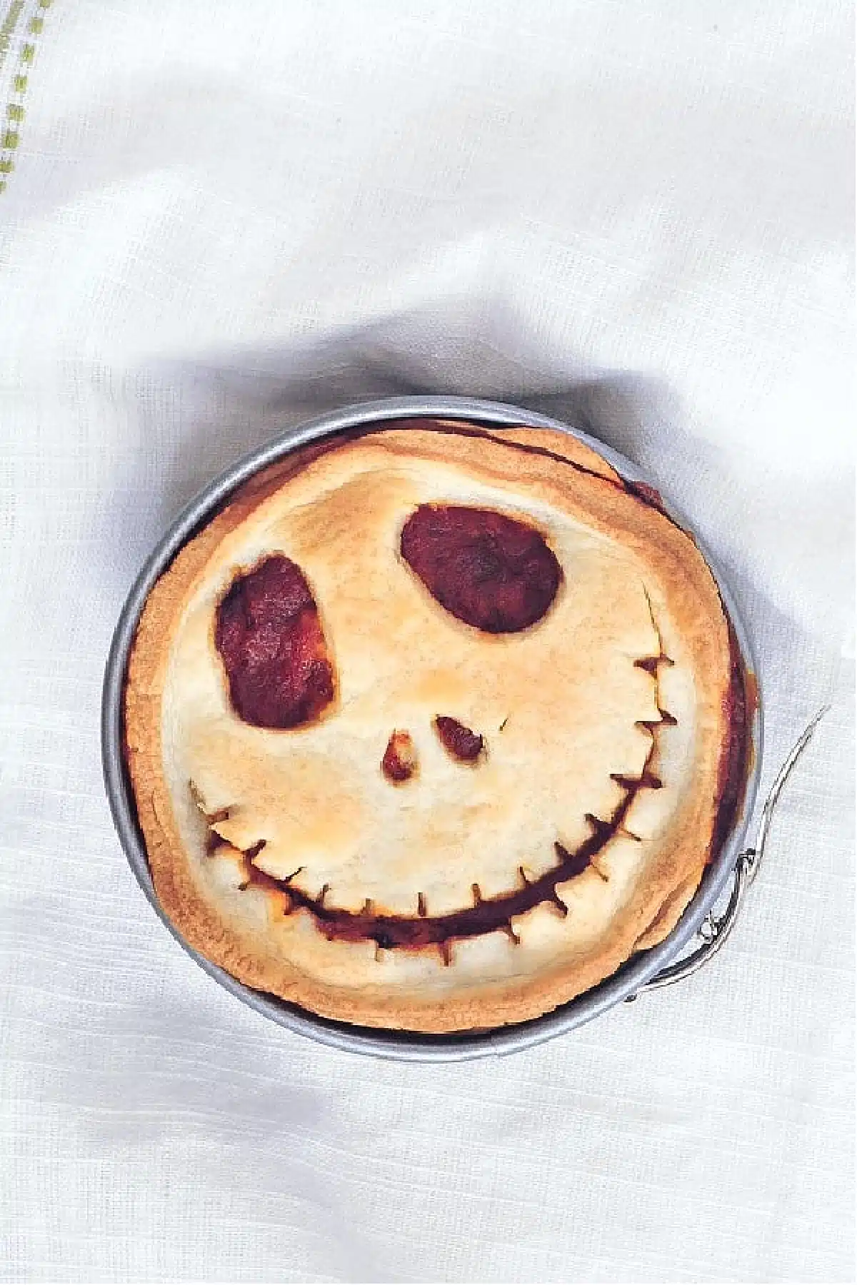 An overhead view of a mini pizza pot pie in a springform pan, the top of the pie cut into a Halloween Jack Skellington skeleton face.