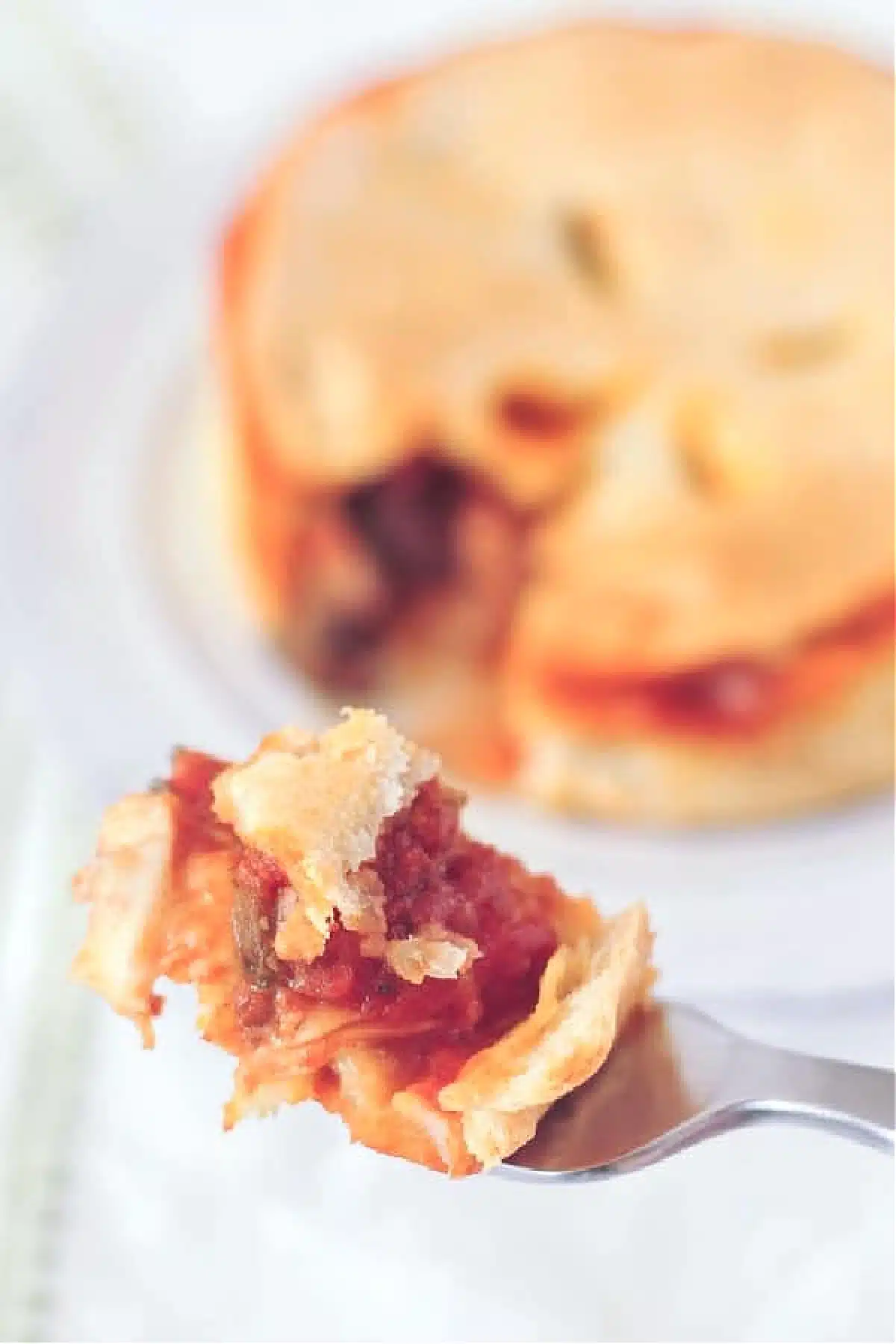 One bite of pizza pot pie on a fork, the pie blurred in background.