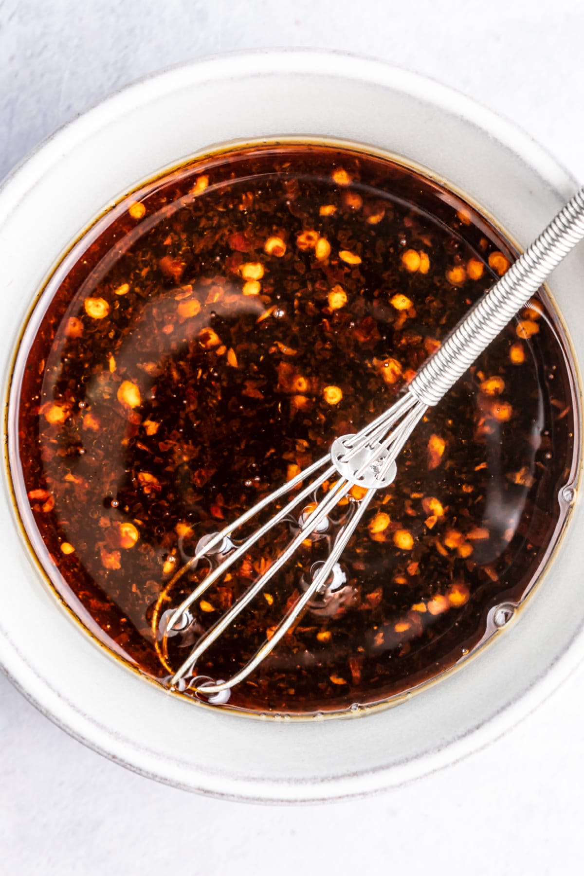 Overhead view of dark brown colored Asian salad dressing in a white bowl with a small silver whisk inside.