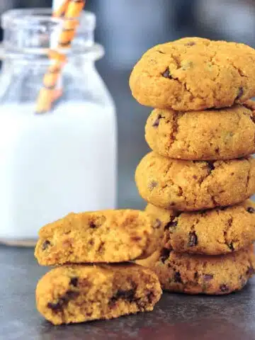 Soft gluten free pumpkin cookies in a stack, next to a short bottle of almond milk with striped straws.